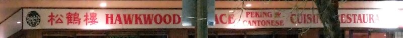 The lit white fascia at night, lettered in red: three Chinese characters, then HAWKWOOD PALACE, PEKING AND CANTONESE CUISINE, RESTAURANT. A light pole and a bare tree cross in front of it.